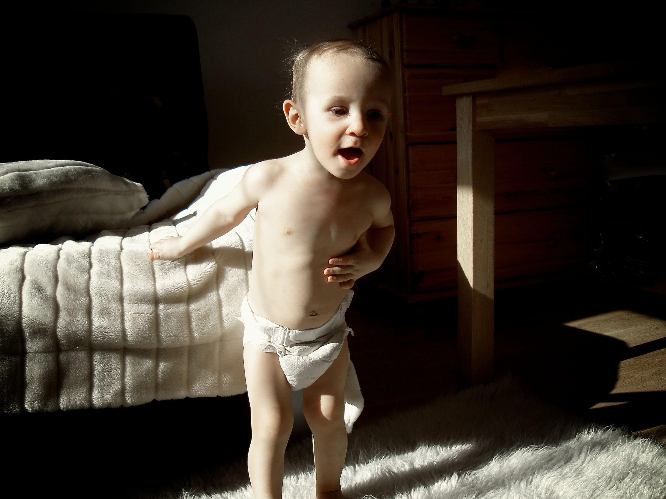 small boy in white briefs standing by the bed