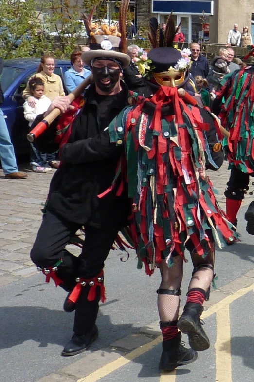 two men dancing in a street parade wearing costumes with feather decorations