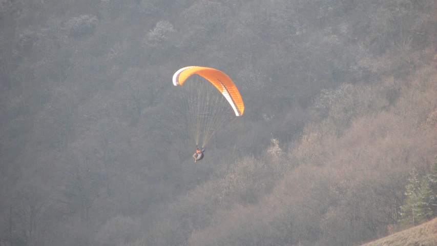 two paragliders flying over the foggy hillside