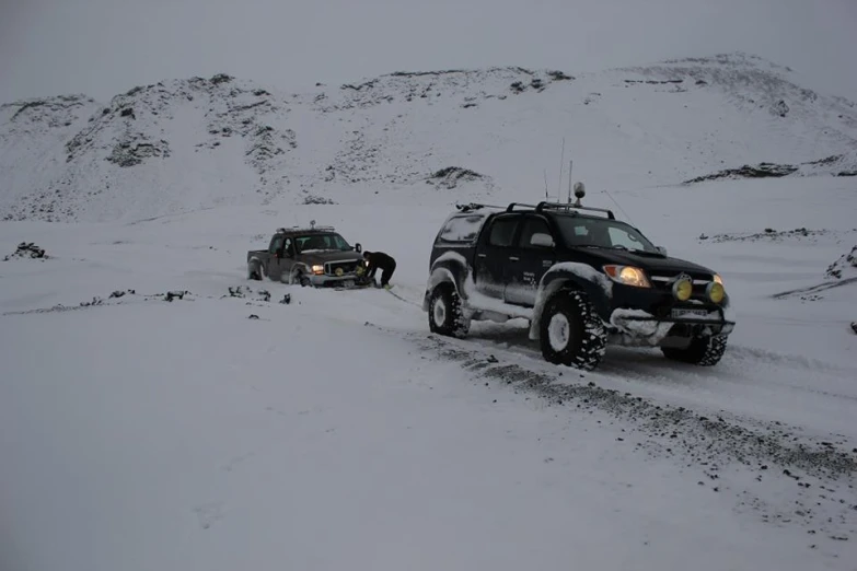 two vehicles drive down a snowy mountain side