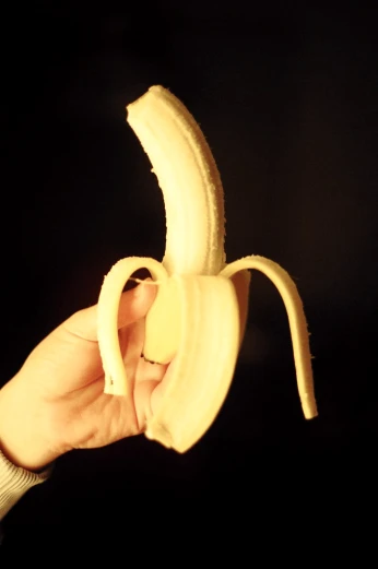 hand holding up half peeled banana over black background