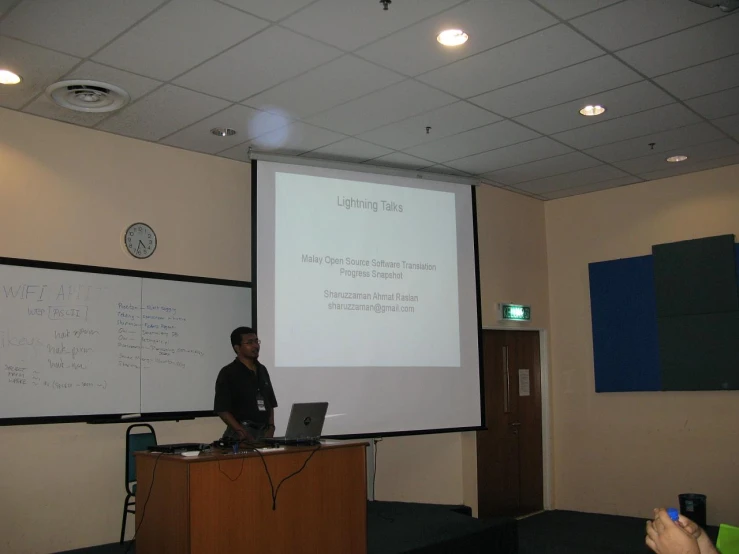 two people are standing at a conference table next to a projector screen and laptop