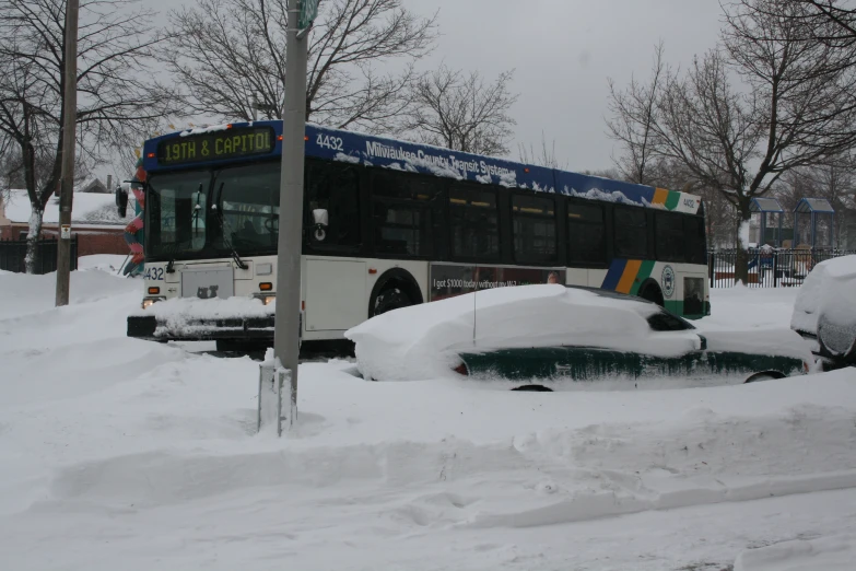 a city bus parked next to a car in a parking lot covered in snow