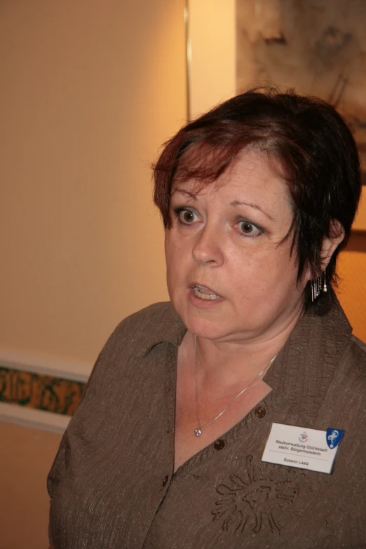 a woman wearing a name tag stands in front of a painting