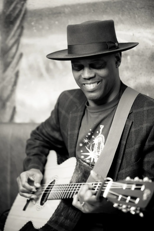 a black man playing an acoustic guitar while wearing a hat