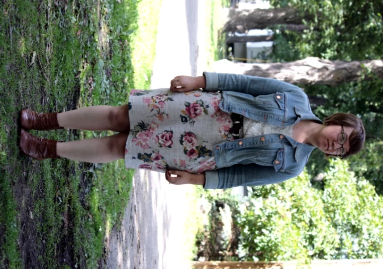 a woman standing in a park wearing a floral skirt and denim jacket