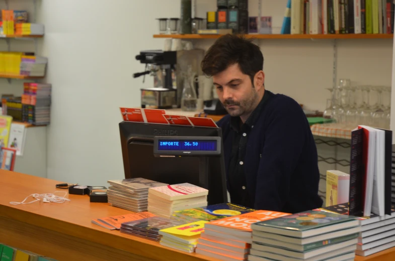 a man sitting at a counter with a clock and stacks of books