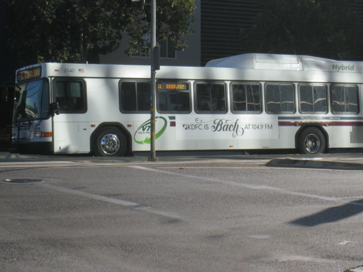 white city bus with advertits parked in the middle of a street
