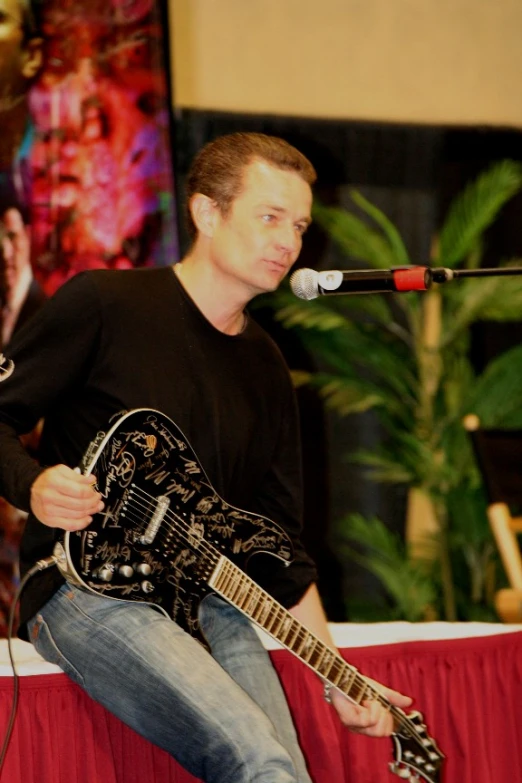 a man with a black guitar sitting on a stage