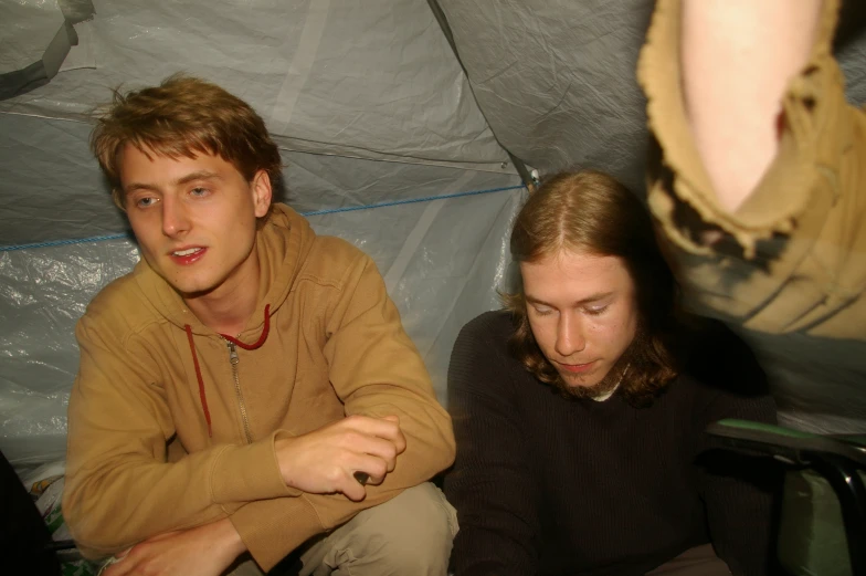 two people sitting in a tent using cellphones