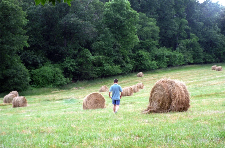 a man walking past large bales of hay
