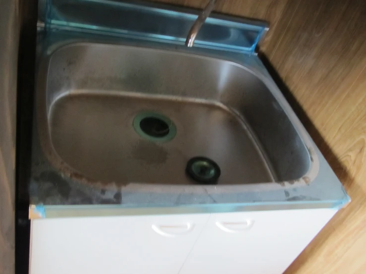 a silver sink under a white cabinet and brown wooden floors