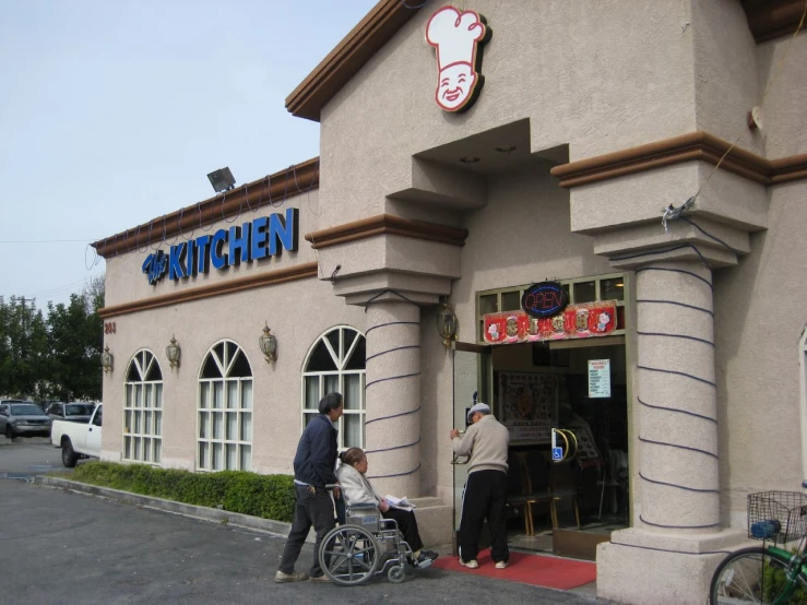 people are outside of a restaurant with a man hing a small child on a wheelchair in front