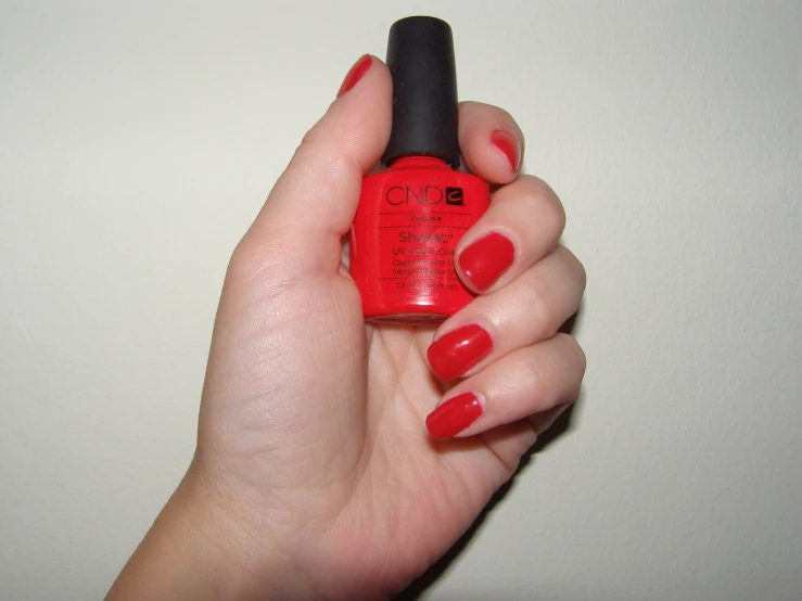 a woman with red nail polish holding onto a red nail bottle