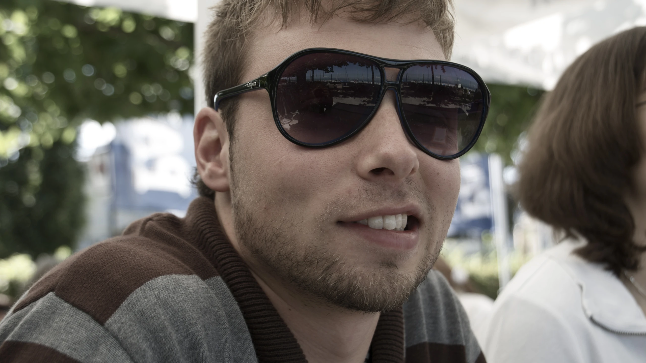 man wearing sunglasses on sunny day with woman in background