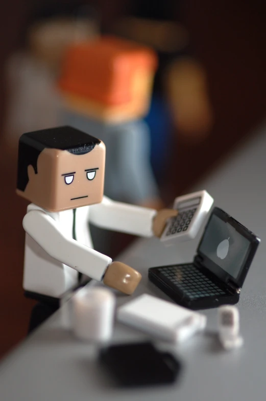 a small toy character holding up an open laptop