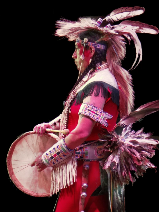 a man dressed in costume and feathers holds drums