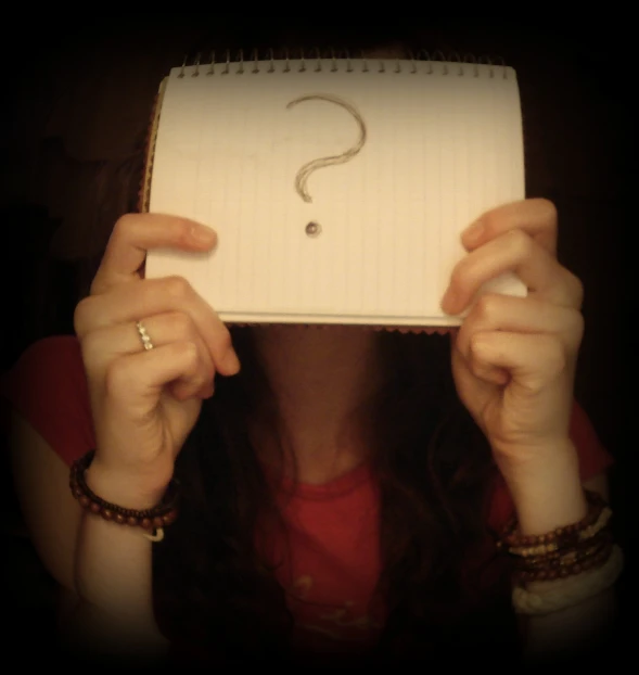 a woman covering her face with her hand and holding up a piece of paper that says question?