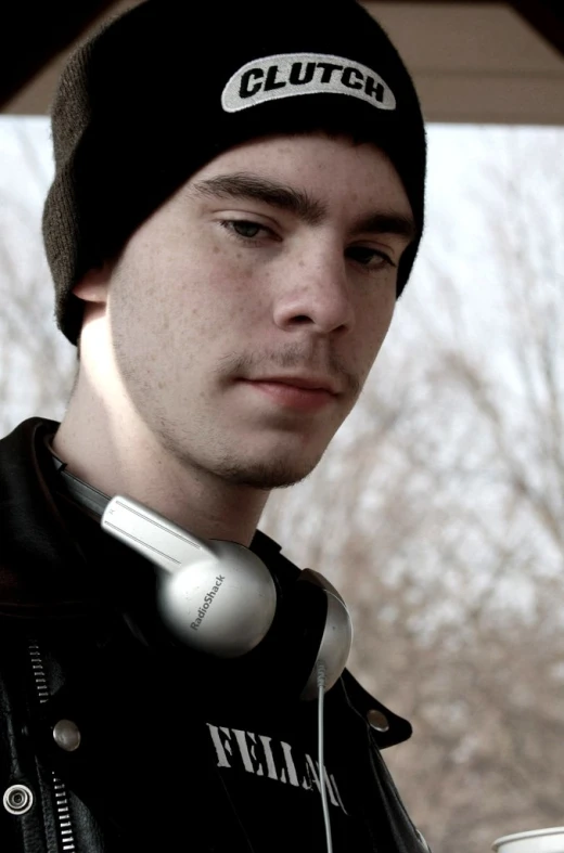 a young man with ear phones wearing a black jacket and a hat