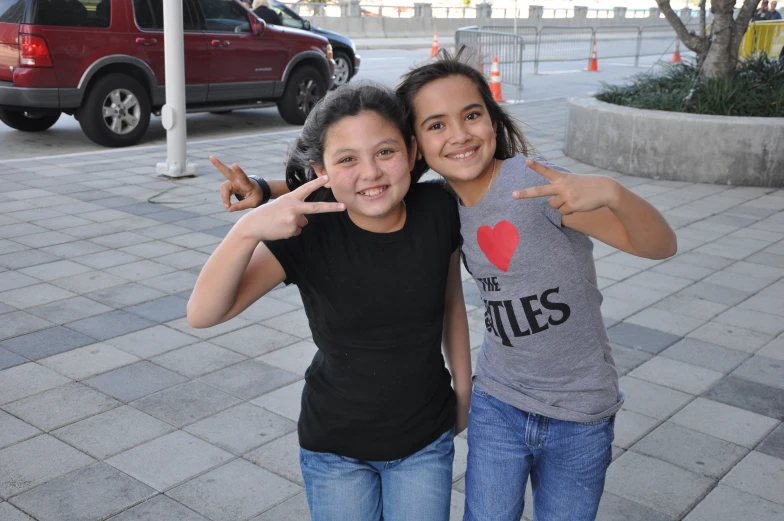 two girls standing in front of a car making peace