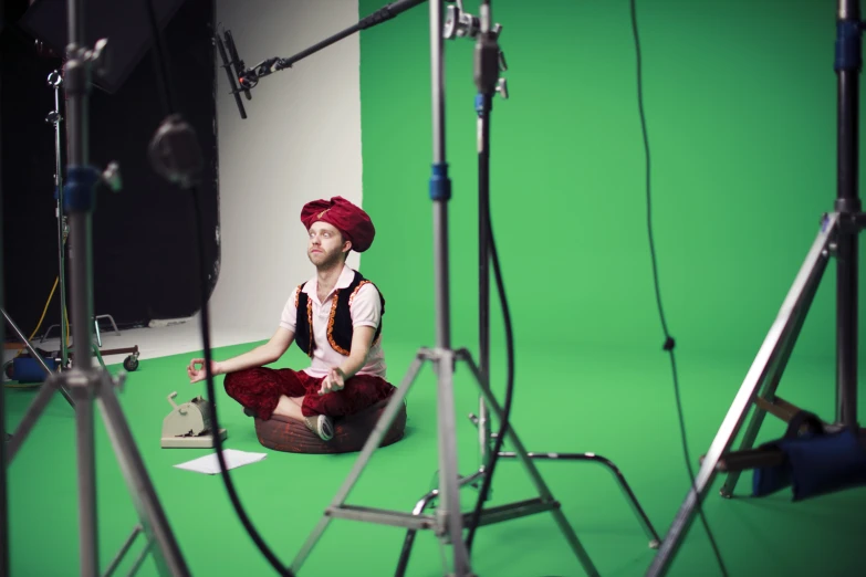 a man in an orange turban sits in front of camera equipment