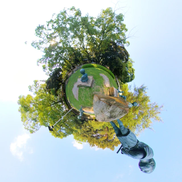 the view from below of a sculpture shows a person in a park setting with various trees