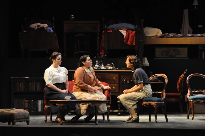 three women sit in chairs and talk on stage