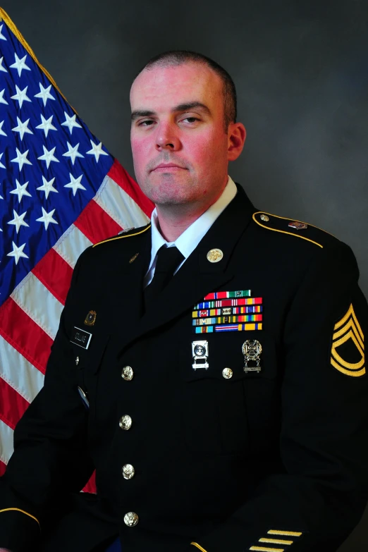 a male in military dress uniform with an american flag behind him