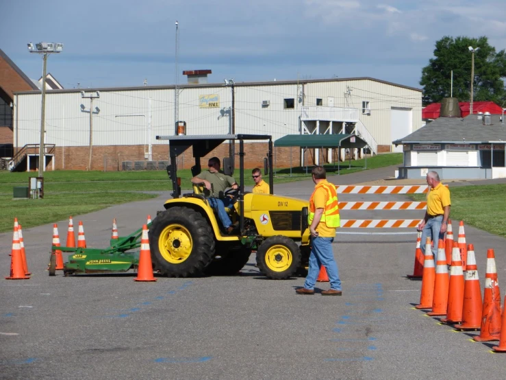 two men are driving a yellow tractor through an orange cones