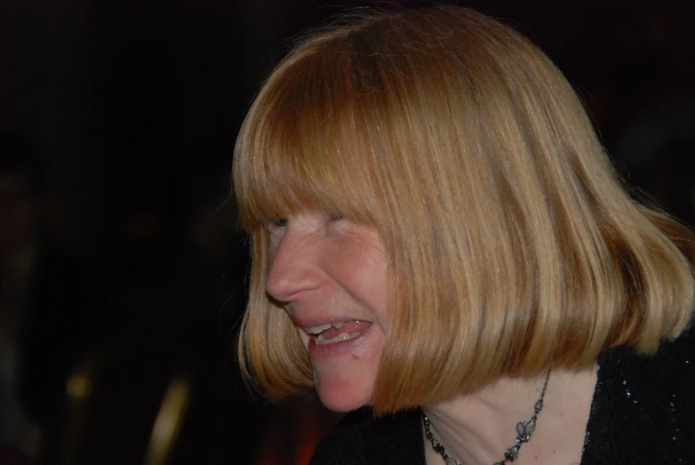 a smiling woman wearing a black jacket with her bangs styled