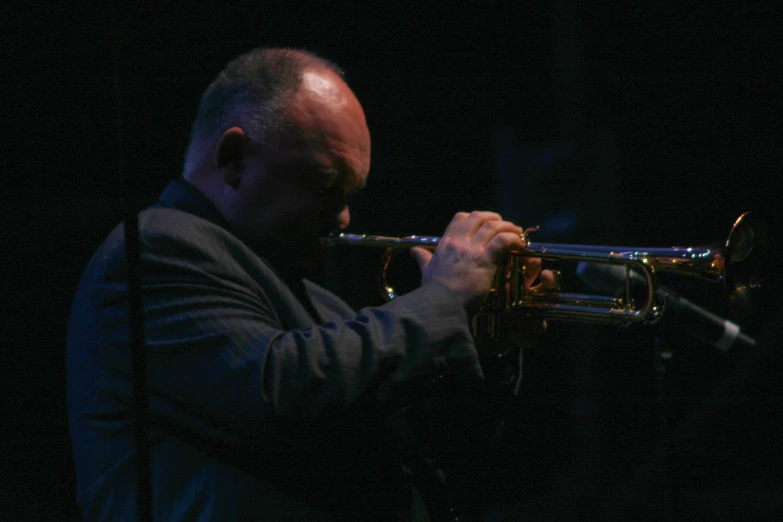 man playing trumpet in dark area with black background