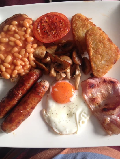 a plate full of breakfast food including eggs, sausage, beans, toast and tomato