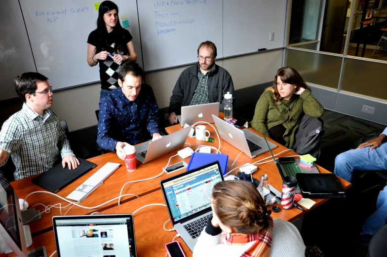 a group of people sitting at a table working on laptops