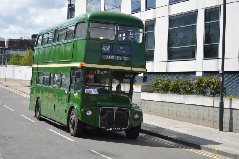 a green double decker bus is stopped on the side of a street