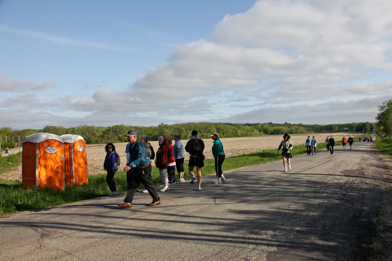 people are walking on the road near a portable toilet