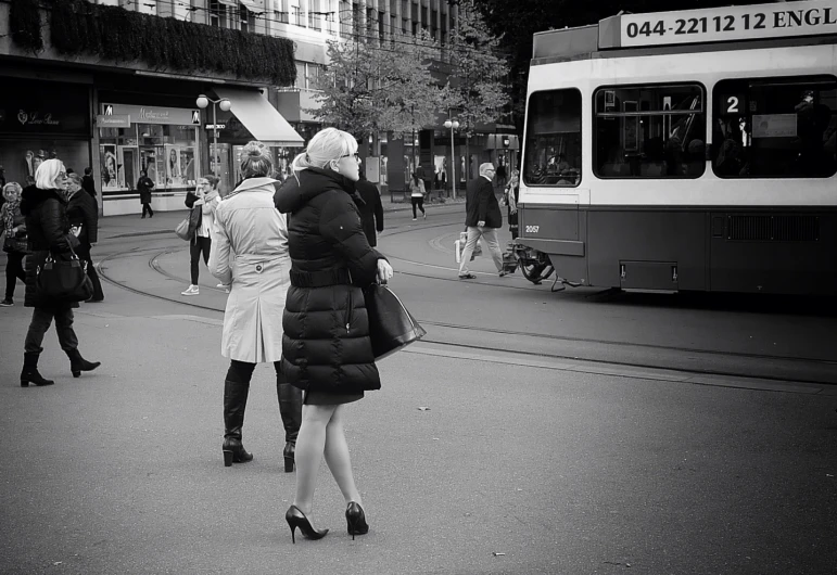 a woman in heels and a coat standing in front of a bus