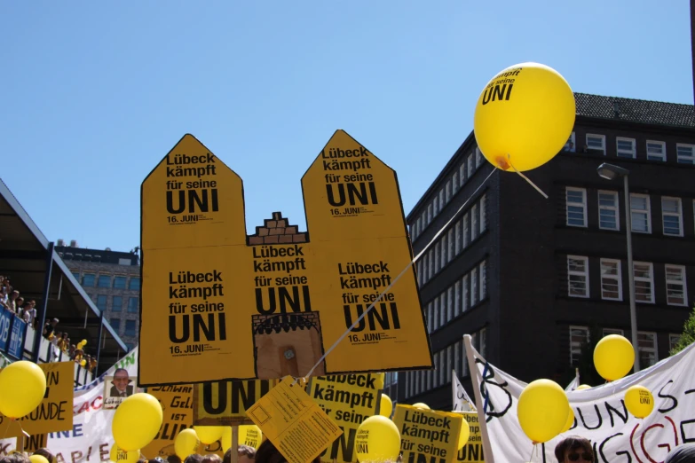 a group of people holding yellow and black signs and balloons