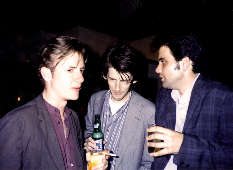 three guys drinking beer while one looks at his cell phone