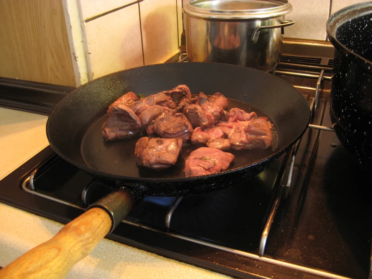there is a large black pan on top of the stove with meat