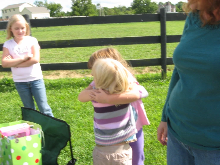 two girls standing next to a fence, with one  holding her arms out and the other woman hugging her