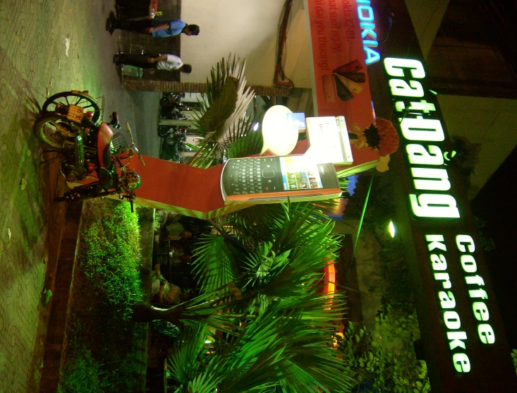 a city street with green plants and a bright sign