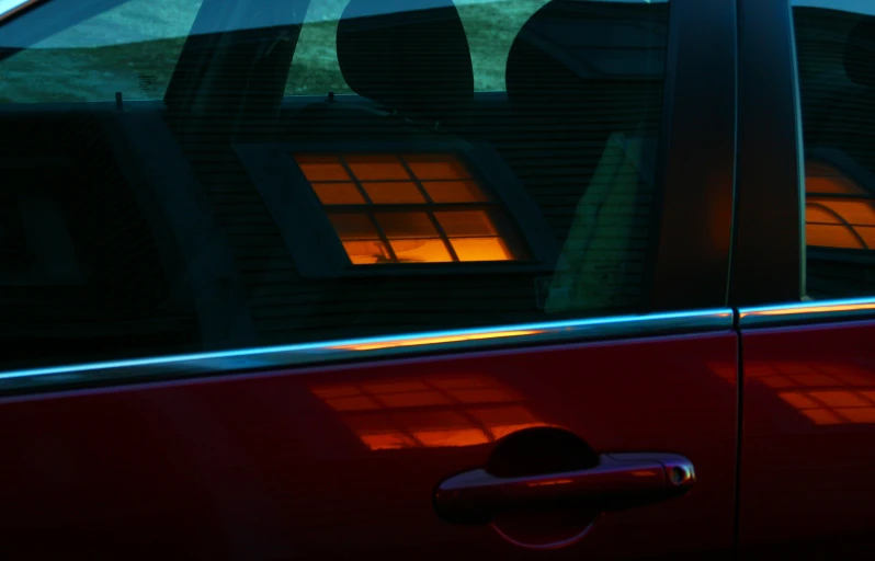 a red car is parked in front of a house with lights coming from the windows