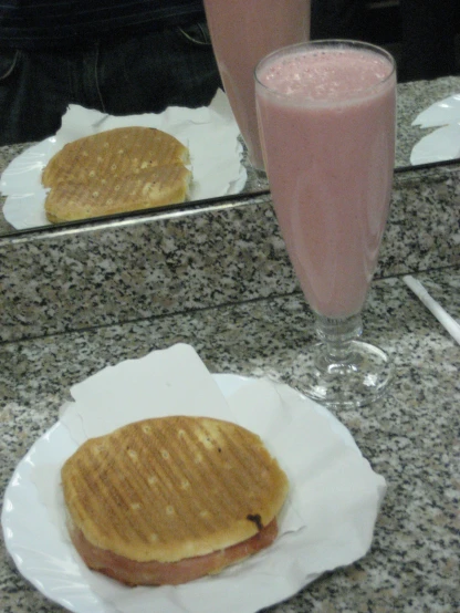 a glass with a milkshake next to a plate with an sandwich