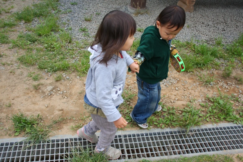 two small children standing in grass by a drain