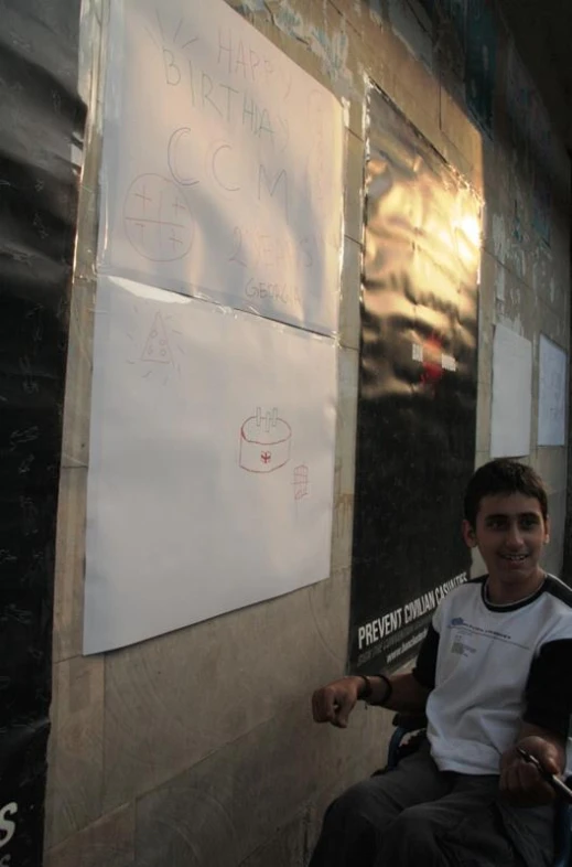 a young man smiles while sitting next to some posters