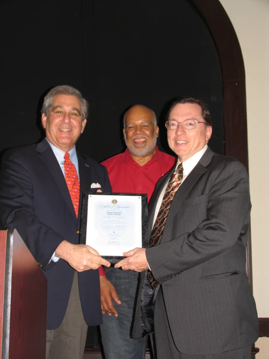 two men are posing for the camera holding a plaque