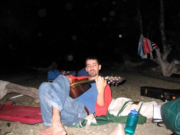 a man plays a guitar while resting on the beach