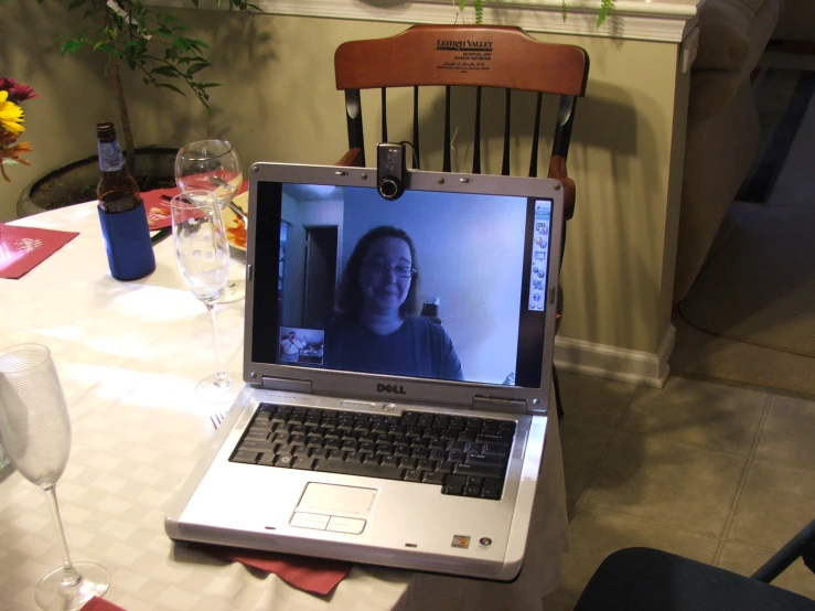an open laptop sitting on a dining room table with a woman on the screen