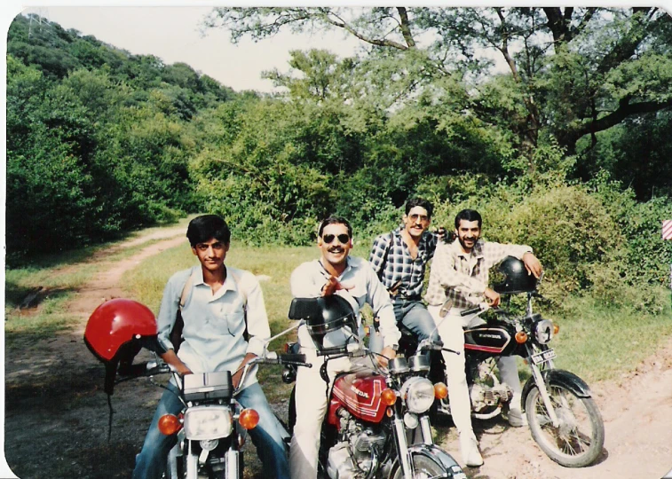 four young men are sitting on bikes near a trail