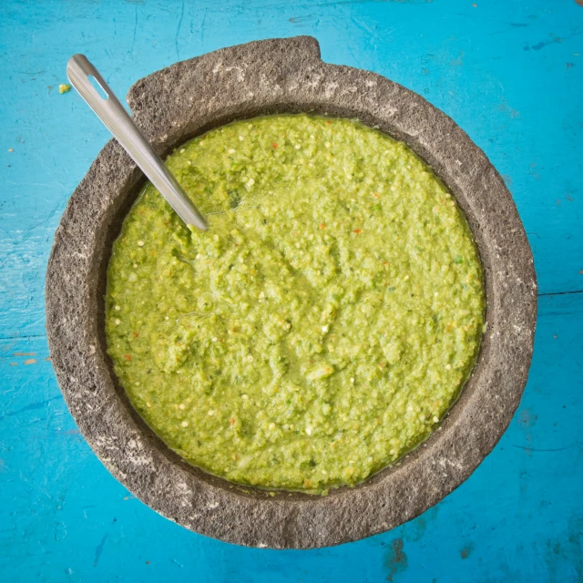 a bowl filled with green dip next to a spoon